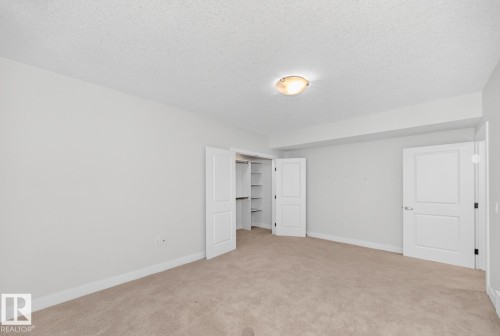 Recessed closet with built-in shelving, panel doors, neutral carpeting, and a flush-mount ceiling light - #57 18343 Lessard Rd Nw, Edmonton, AB - Indoor Photo Showing Other Room