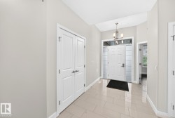 Front entry featuring a paneled door with frosted glass sidelights and transom, a brushed nickel chandelier, and light-toned tile flooring - 