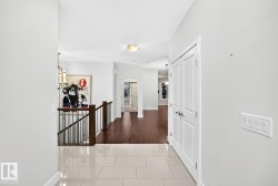 Tiled flooring, warm wood-finish flooring, white paneled doors, and a staircase with wood handrails and black metal balusters - 