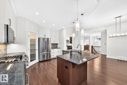 Open-concept kitchen featuring a dark wood-finish island with a stone countertop, stainless steel appliances, white cabinetry, and wood-finish flooring - 