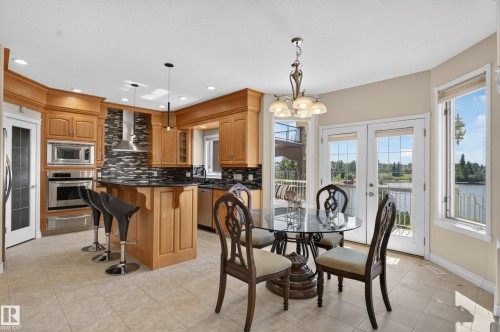 Kitchen with wood cabinetry, stainless steel appliances, a black tile backsplash, and a breakfast bar - 13527 158 Avenue Nw, Edmonton, AB - Indoor Photo Showing Dining Room