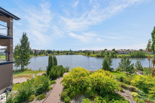 Expansive lakefront setting with lush landscaping, a winding brick paver pathway, and a multi-level balcony featuring glass railings - 13527 158 Avenue Nw, Edmonton, AB - Outdoor With Body Of Water With View
