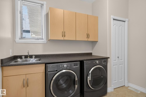 Utility room featuring a stainless steel sink, wood-finish cabinetry, dark countertop, and a white paneled door - 13527 158 Avenue Nw, Edmonton, AB - Indoor Photo Showing Laundry Room