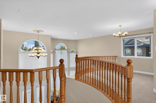 Curved wood-finish staircase with balusters, arched windows with blinds, and decorative chandeliers - 13527 158 Avenue Nw, Edmonton, AB - Indoor Photo Showing Other Room