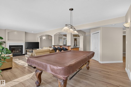 Wood-finish flooring throughout, recessed lighting, arched doorways, a built-in fireplace with a mantel, and an integrated bar area - 13527 158 Avenue Nw, Edmonton, AB - Indoor Photo Showing Other Room With Fireplace