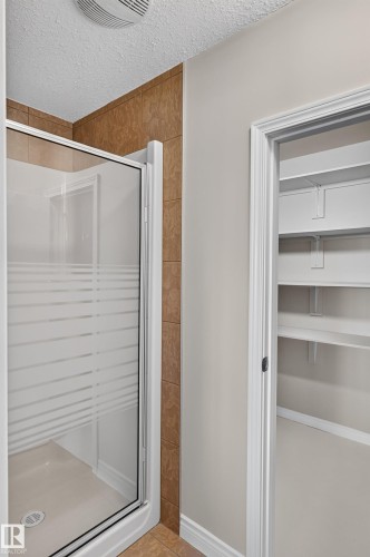 Walk-in shower with frosted glass enclosure, tile surround, and an adjacent built-in closet with shelving - 13527 158 Avenue Nw, Edmonton, AB - Indoor