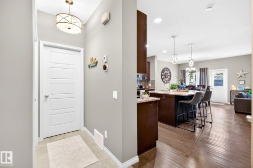 Open-concept living space with dark wood-finish flooring, a kitchen island with seating, a dining area, and a white paneled door - 16512 140 Street Nw, Edmonton, AB - Indoor