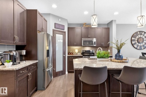 Dark wood-finish cabinetry with stainless steel appliances, light-toned granite countertops, and wood-finish flooring - 16512 140 Street Nw, Edmonton, AB - Indoor Photo Showing Kitchen With Upgraded Kitchen