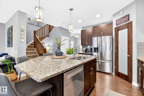 Kitchen island with an undermount double basin sink, stainless steel dishwasher, and seating for three - 16512 140 Street Nw, Edmonton, AB - Indoor Photo Showing Kitchen With Double Sink With Upgraded Kitchen
