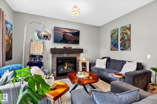 Living area featuring a gas fireplace with a stone surround, a dark wood mantel, light-toned walls, and a ceiling-mounted light fixture - 16512 140 Street Nw, Edmonton, AB - Indoor Photo Showing Living Room With Fireplace