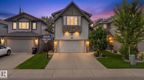Exterior featuring a stone facade, wood-look siding, attached two-car garage, concrete driveway, and manicured landscaping - 16512 140 Street Nw, Edmonton, AB - Outdoor With Facade