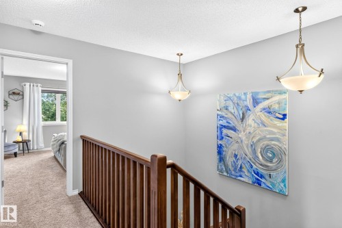 Staircase with wood balusters and handrail, neutral wall color, and two ceiling-mounted pendant lights - 16512 140 Street Nw, Edmonton, AB - Indoor Photo Showing Other Room