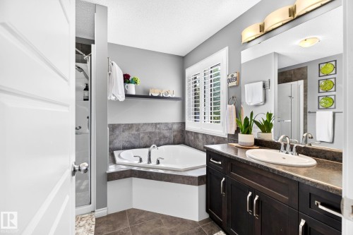 Recessed corner soaking tub, dark wood-finish vanity with an undermount sink, plantation shutters, and a walk-in shower with a glass enclosure - 16512 140 Street Nw, Edmonton, AB - Indoor Photo Showing Bathroom
