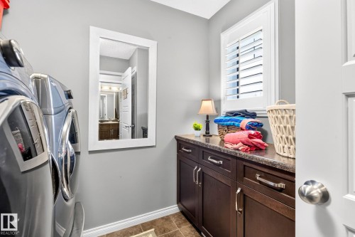Laundry area featuring stacked appliances, dark wood-finish cabinetry, a patterned countertop, and a window with white louvered shutters - 16512 140 Street Nw, Edmonton, AB - Indoor Photo Showing Laundry Room