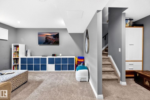 Wall-mounted television with built-in storage shelving, light-toned carpeting, recessed ceiling lighting, and a carpeted staircase - 16512 140 Street Nw, Edmonton, AB - Indoor