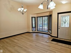 Wood-finish flooring, bay window with blinds, decorative front entry door, and two chandelier light fixtures - 