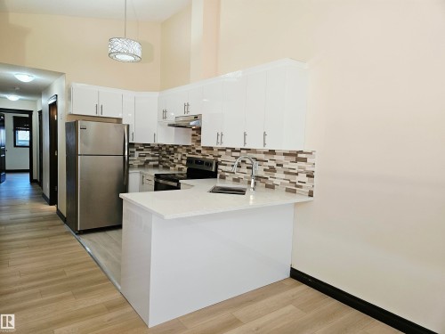 Kitchen featuring wood-finish flooring, white cabinetry, a mosaic tile backsplash, and stainless steel appliances - 11625 88 Street Nw, Edmonton, AB 