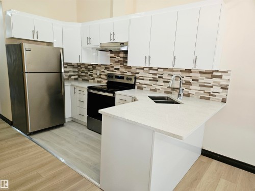 Kitchen featuring white cabinetry, stainless steel appliances, a mosaic tile backsplash, and light-toned countertops - 11625 88 Street Nw, Edmonton, AB 