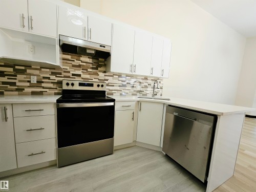 Kitchen featuring white cabinetry, light-toned countertops, a mosaic tile backsplash, stainless steel appliances, and wood-finish flooring - 11625 88 Street Nw, Edmonton, AB 