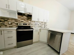 Kitchen featuring white cabinetry, light-toned countertops, a mosaic tile backsplash, stainless steel appliances, and wood-finish flooring - 