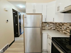 Stainless steel refrigerator, white cabinetry with silver hardware, light-toned countertop, and mosaic tile backsplash - 