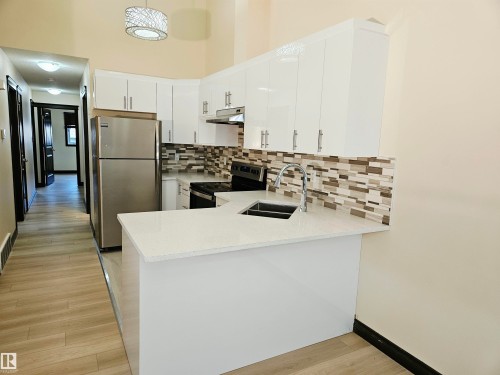 Kitchen featuring white cabinetry, light-colored countertops, stainless steel appliances, and a mosaic tile backsplash - 11625 88 Street Nw, Edmonton, AB 
