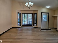 Wood-finish flooring, bay window with blinds, decorative front door, vaulted ceiling, and built-in shelving - 