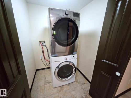 Dedicated laundry area with stacked front-load washer and dryer, tile flooring, and dark paneled doors - 11625 88 Street Nw, Edmonton, AB 