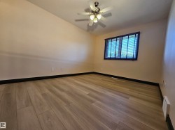 Wood-finish flooring with dark baseboards, a ceiling fan with integrated lighting, and a window with blinds - 