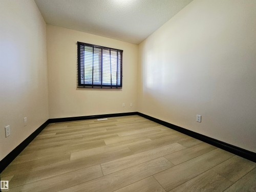Neutral tone wall finish with dark baseboards, light wood-finish flooring, and a single window with dark blinds - 11625 88 Street Nw, Edmonton, AB 