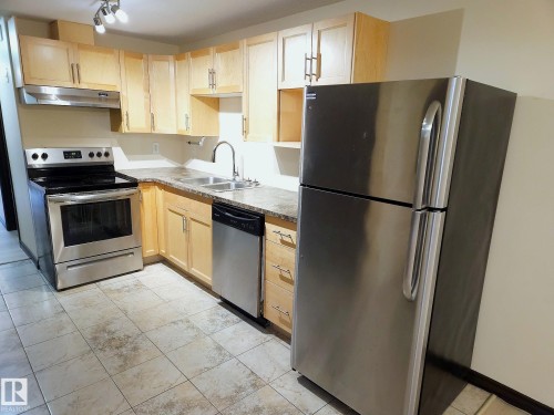 Kitchen featuring light wood cabinetry, stainless steel appliances, a double basin sink, stone-look countertops, and tiled flooring - 11625 88 Street Nw, Edmonton, AB 