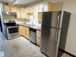 Kitchen featuring light wood cabinetry, stainless steel appliances, a double basin sink, stone-look countertops, and tiled flooring - 