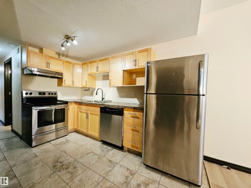 Kitchen featuring light wood cabinetry, stone-finish countertops, stainless steel appliances, and tiled flooring - 11625 88 Street Nw, Edmonton, AB 