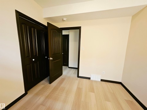 Cream-painted walls, dark wood-finish trim, light wood-finish flooring, dark wood-finish paneled doors, and white door hardware - 11625 88 Street Nw, Edmonton, AB 