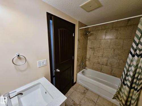 Bathtub with shower, tile surround, integrated sink with modern faucet, and dark wood-finish paneled door - 11625 88 Street Nw, Edmonton, AB 