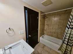 Bathtub with shower, tile surround, integrated sink with modern faucet, and dark wood-finish paneled door - 