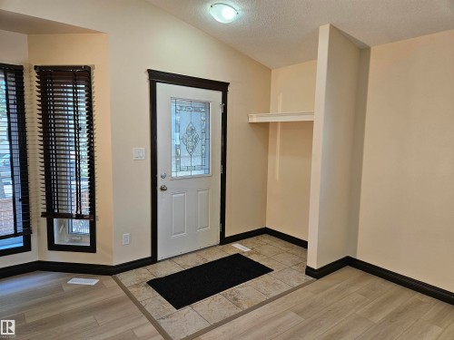 Foyer featuring a decorative glass panel entry door, vaulted ceiling, built-in shelving, and mixed flooring with tile and wood-finish planks - 11625 88 Street Nw, Edmonton, AB 