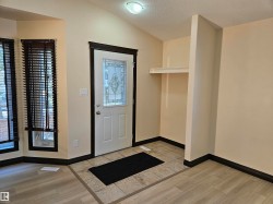 Foyer featuring a decorative glass panel entry door, vaulted ceiling, built-in shelving, and mixed flooring with tile and wood-finish planks - 