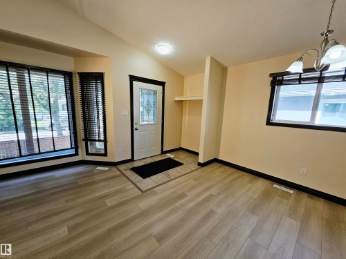Wood-finish flooring throughout, bay window with blinds, front entry door with decorative glass inlay, recessed ceiling light, and a built-in shelving unit - 11625 88 Street Nw, Edmonton, AB 