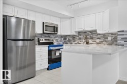 White cabinetry with panel detailing, stainless steel appliances, mosaic tile backsplash, light-toned countertop, and track lighting - 