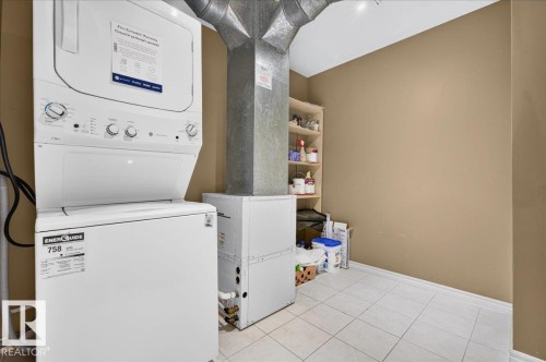 Stackable laundry appliances, white tiled flooring, and built-in shelving - #1102 10909 103 Av Nw, Edmonton, AB - Indoor Photo Showing Laundry Room