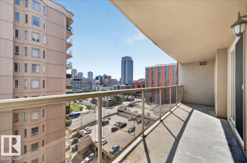 Concrete balcony with glass railing, urban skyline, exterior wall light fixture, and sliding glass door - #1102 10909 103 Av Nw, Edmonton, AB - Outdoor With Balcony With Exterior