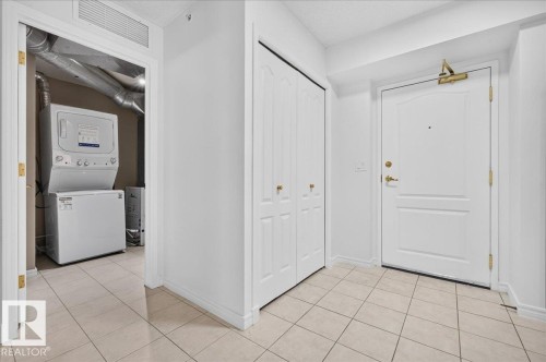 White paneled entry door with brass hardware, stacked laundry appliances, and tile flooring - #1102 10909 103 Av Nw, Edmonton, AB - Indoor Photo Showing Laundry Room
