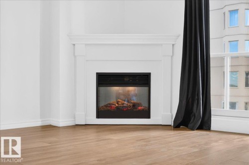 White mantel fireplace with an electric insert, wood-finish flooring, and expansive windows - #1102 10909 103 Av Nw, Edmonton, AB - Indoor Photo Showing Living Room With Fireplace
