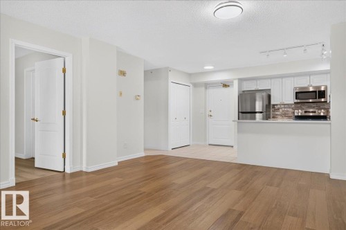 Wood-finish flooring throughout, kitchen with white cabinetry, stainless steel appliances, and a tiled backsplash - #1102 10909 103 Av Nw, Edmonton, AB - Indoor Photo Showing Kitchen