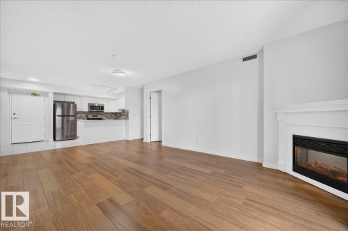 Wood-finish flooring, white walls, and a built-in fireplace with a white mantel - #1102 10909 103 Av Nw, Edmonton, AB - Indoor Photo Showing Living Room With Fireplace