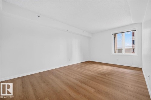 Spacious room featuring wood-finish flooring, white walls, and a large window - #1102 10909 103 Av Nw, Edmonton, AB - Indoor Photo Showing Other Room
