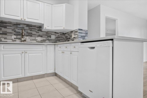 White cabinetry, mosaic tile backsplash, solid surface countertops, integrated dishwasher, and tile flooring - #1102 10909 103 Av Nw, Edmonton, AB - Indoor Photo Showing Kitchen