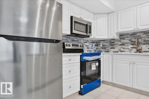 Stainless steel appliances, white cabinetry, integrated microwave, mosaic tile backsplash, and a contemporary faucet - #1102 10909 103 Av Nw, Edmonton, AB - Indoor Photo Showing Kitchen