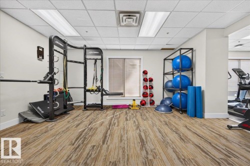 Dedicated fitness area featuring patterned carpet flooring, a power rack, and exercise equipment storage - #1102 10909 103 Av Nw, Edmonton, AB - Indoor Photo Showing Gym Room